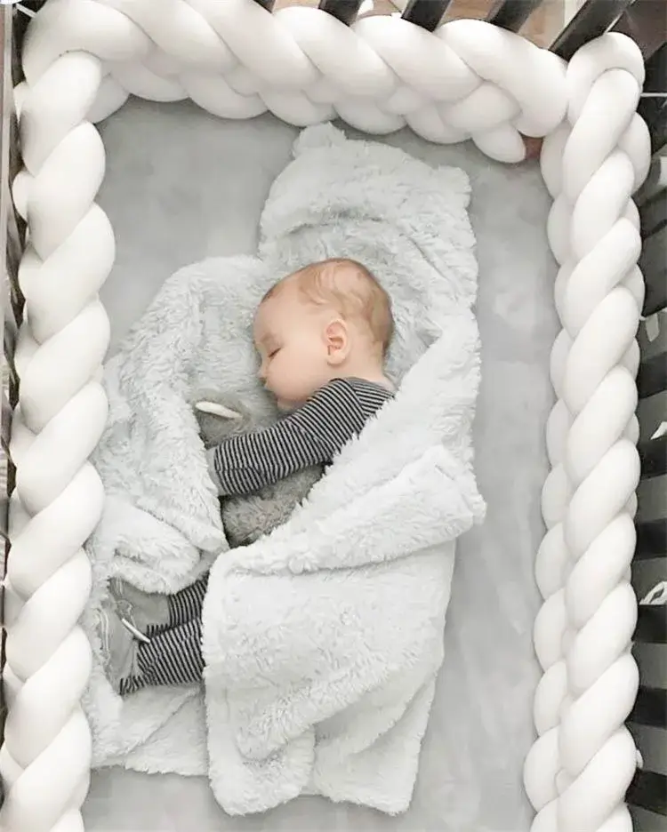Bébé qui dort dans un berceau entouré par un tour de lit tressé blanc
